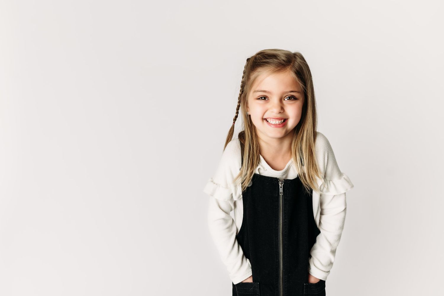 Child in black and white outfit smiling at camera against minimalist white backdrop.