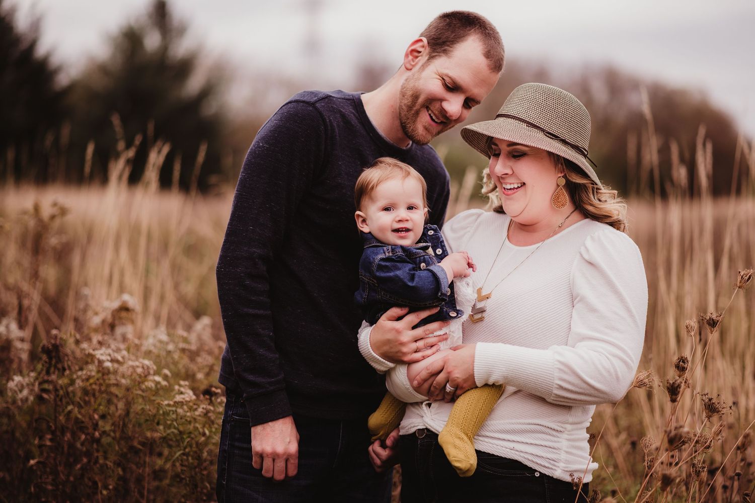Family enjoying a tender moment together in tall autumn grass at sunset.