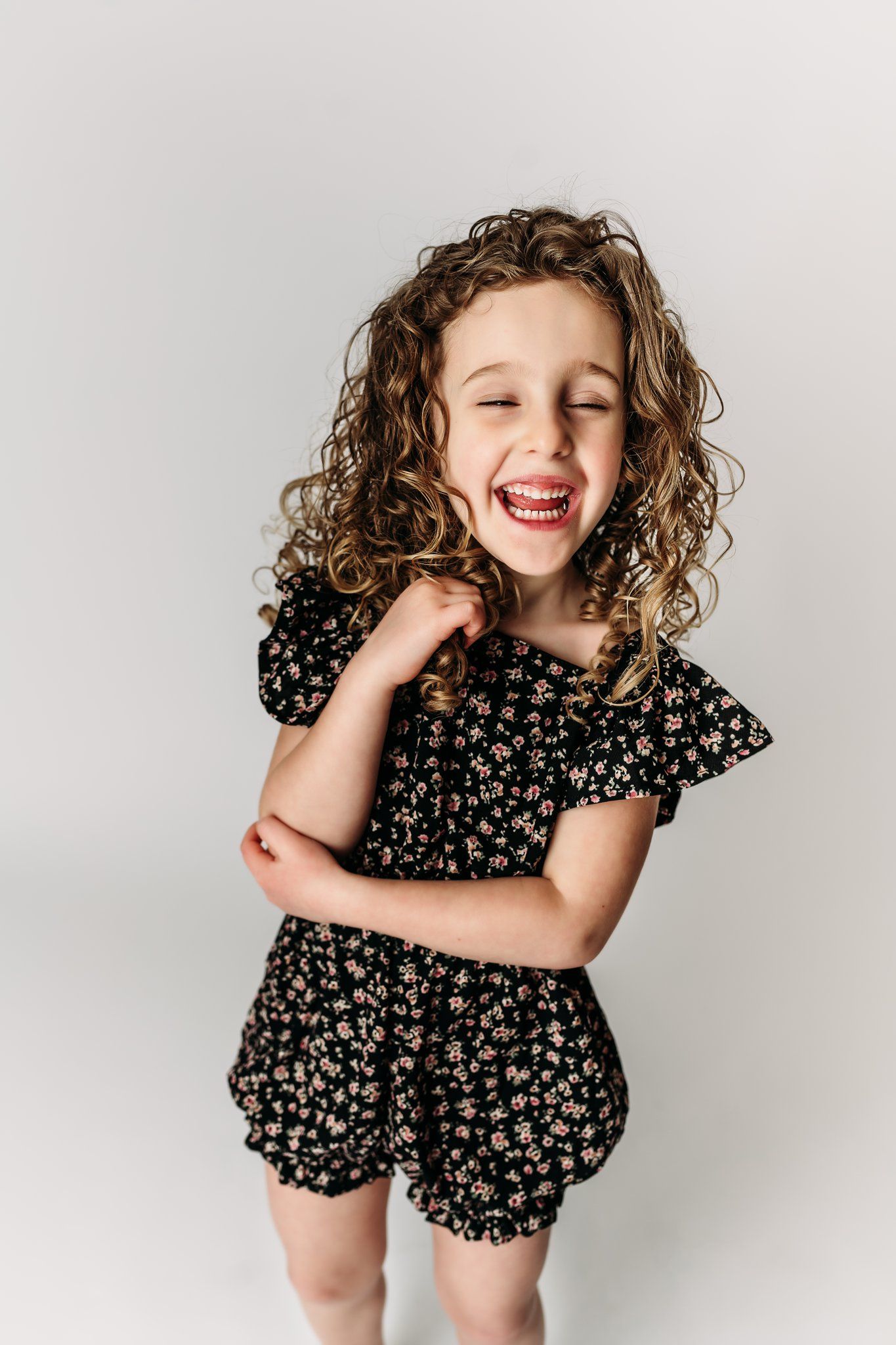 A child laughs joyfully while wearing a dark floral outfit against white background.