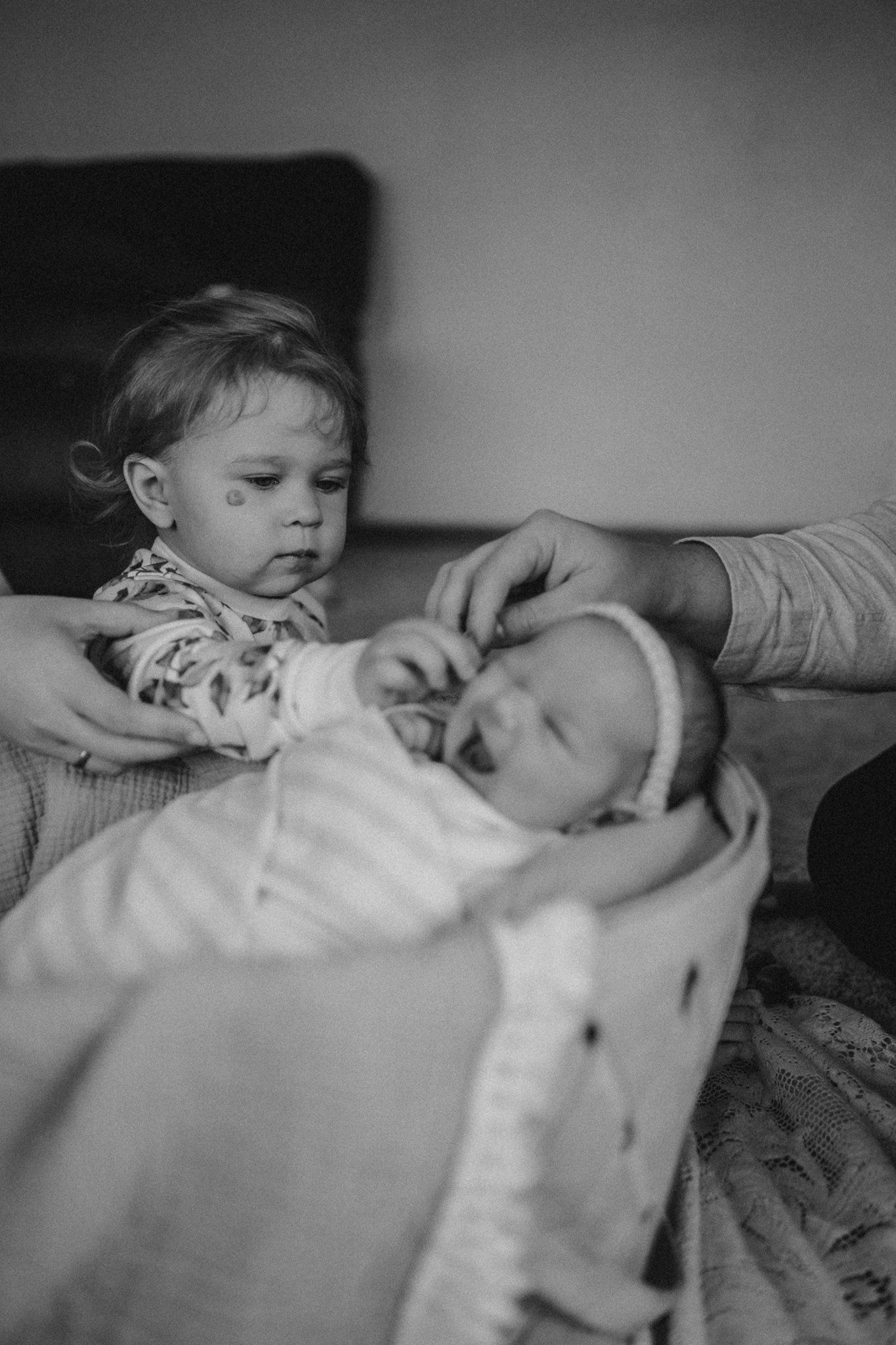 Black and white portrait of tender sibling moment with sleeping infant.