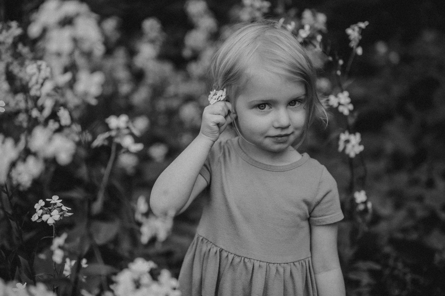 Black and white portrait of child holding flower while standing in garden.