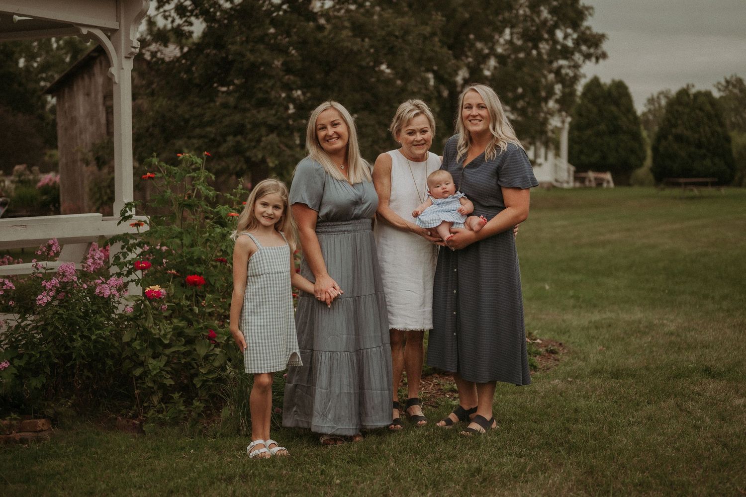 Family group poses together in front of a white gazebo and rose garden at dusk.