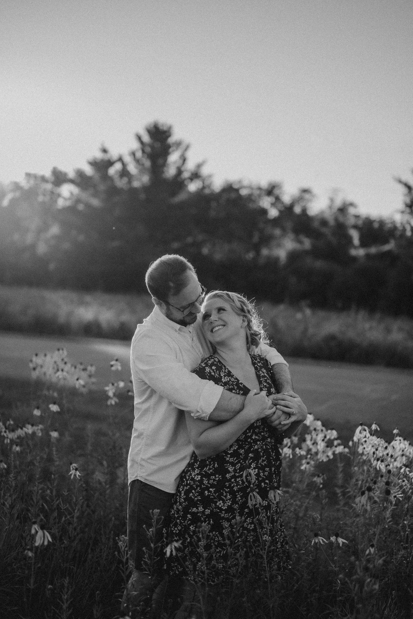 Black and white photo of couple dancing in a flower-filled meadow at dusk.