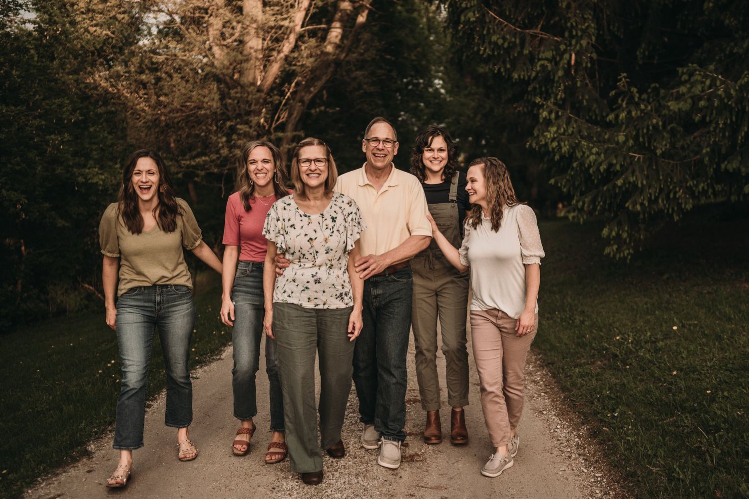 A group of people dressed casually stand together on a tree-lined path during golden hour.