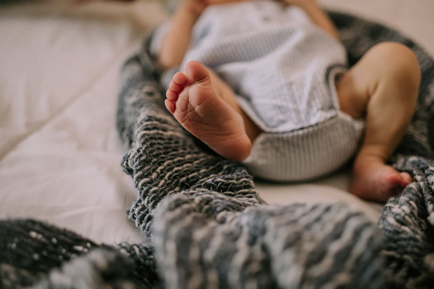 Close-up of tiny baby feet resting on gray knitted blanket.