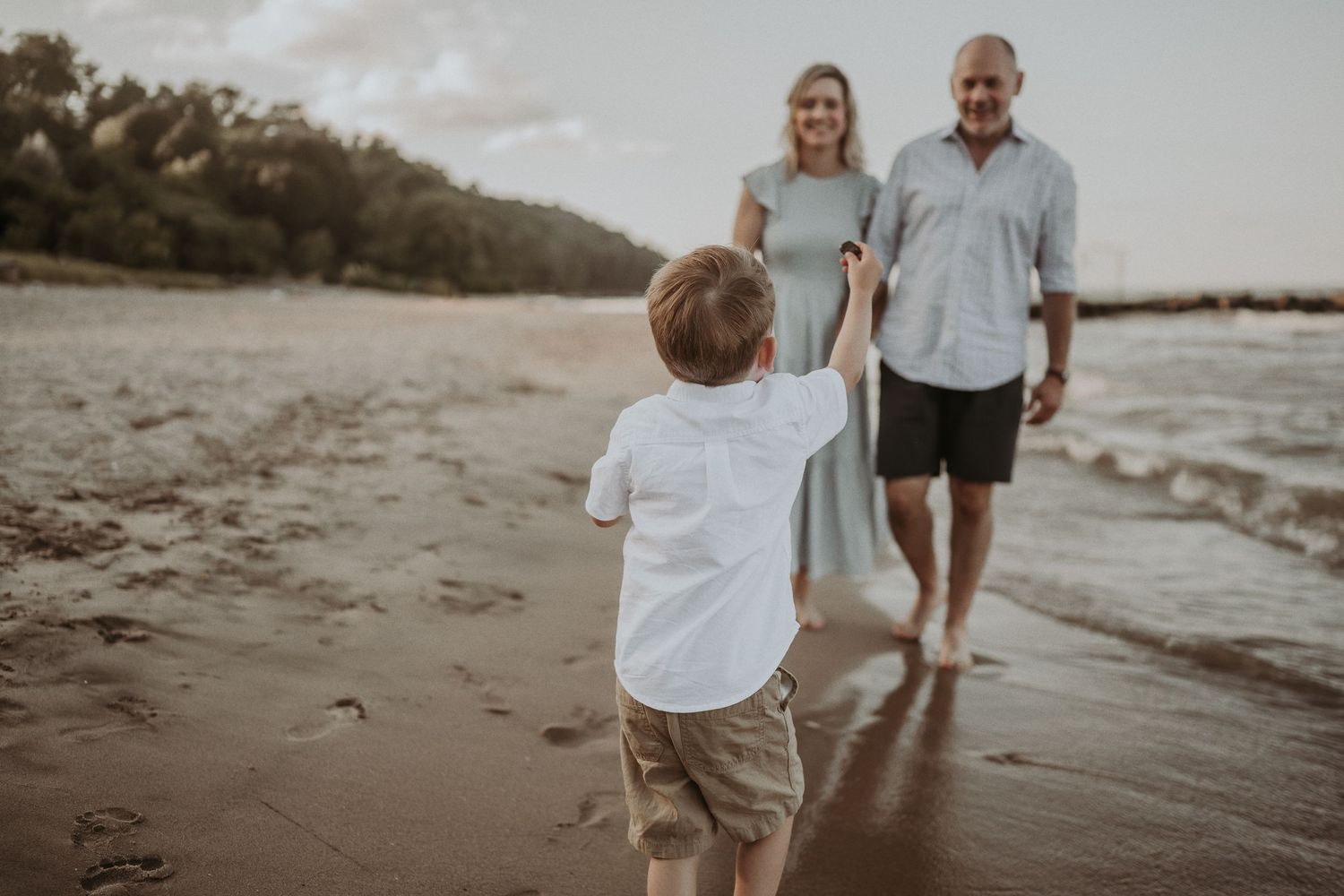 Child in white shirt walking towards two adults on a scenic beach at dusk.