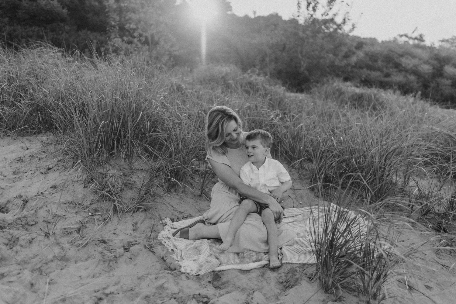 Intimate family moment captured in black and white on sandy beach during sunset.