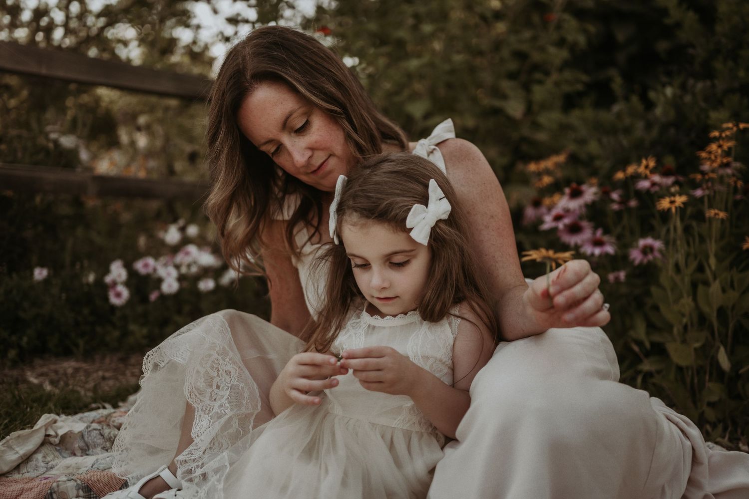 An intimate moment captured between two people in white dresses sitting on floral blanket.