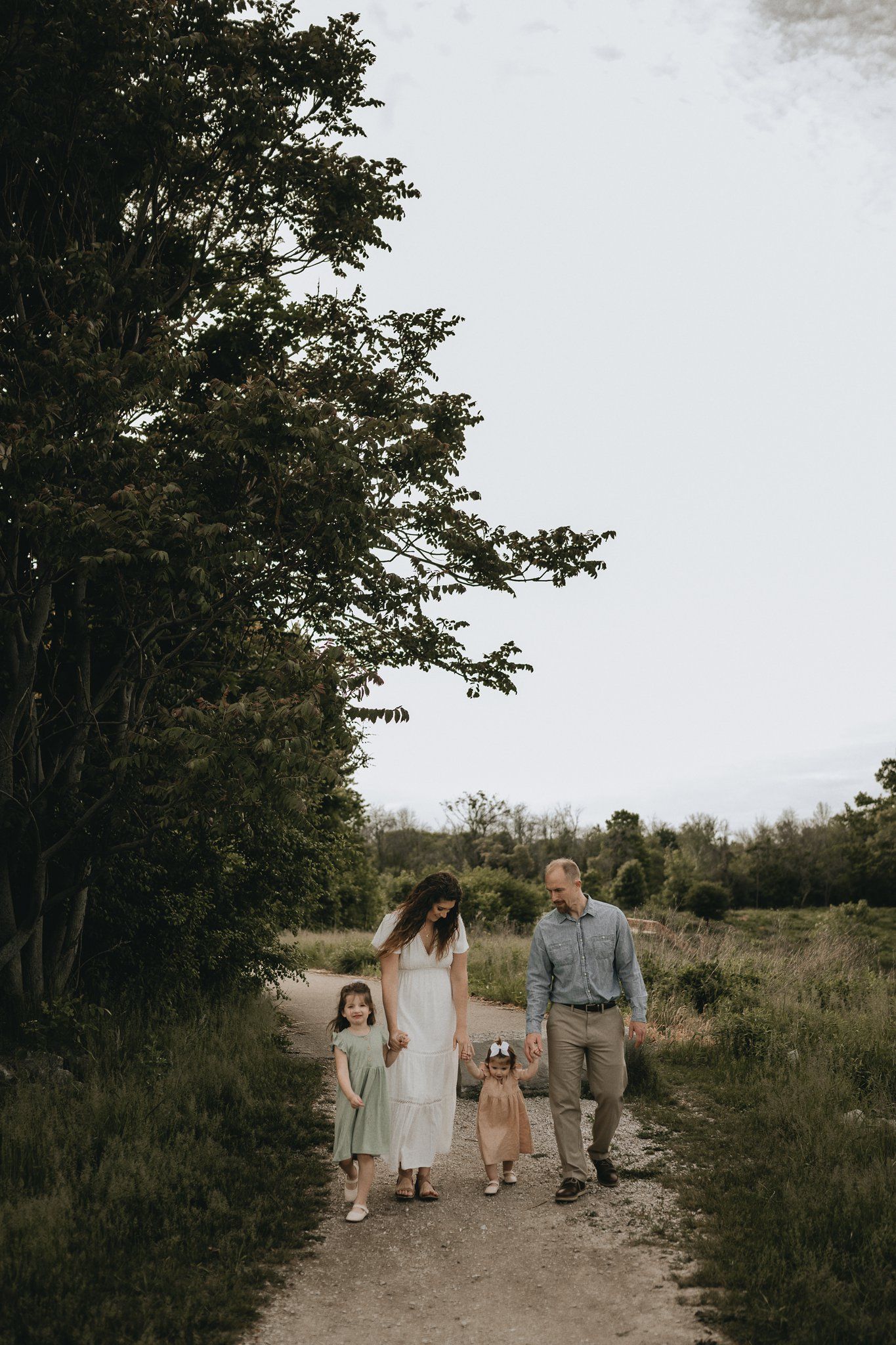 Family walking together on a nature path surrounded by trees during golden hour.