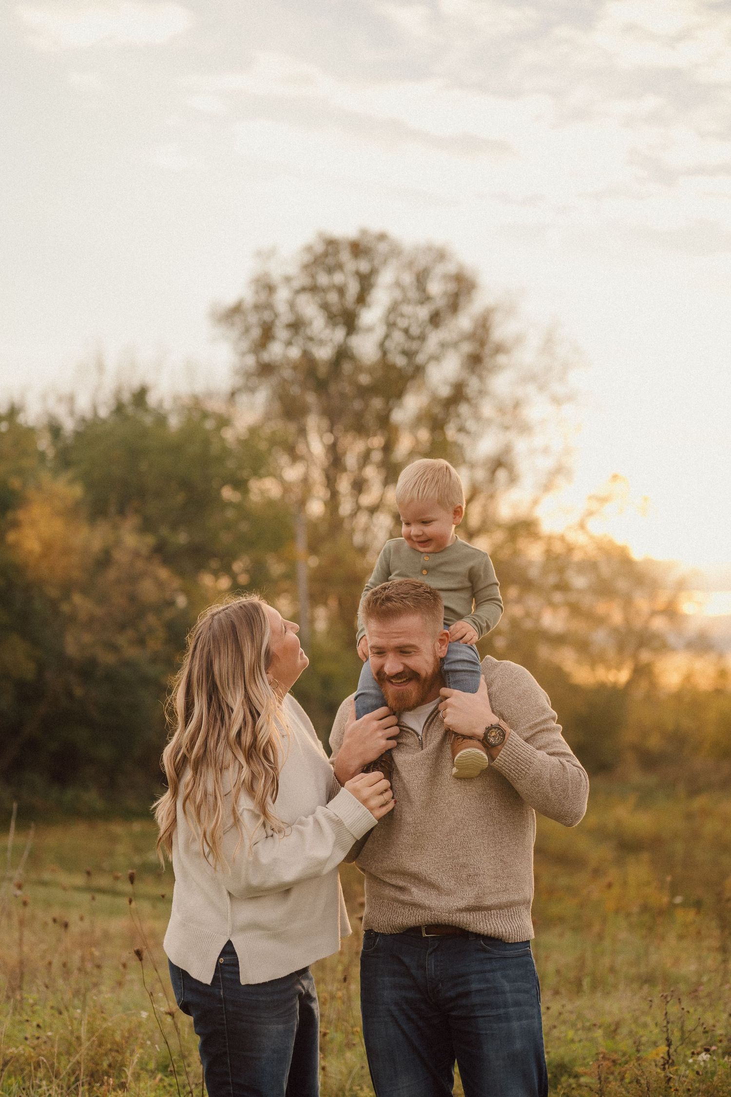 Family plays and laughs together in a golden autumn field at sunset.