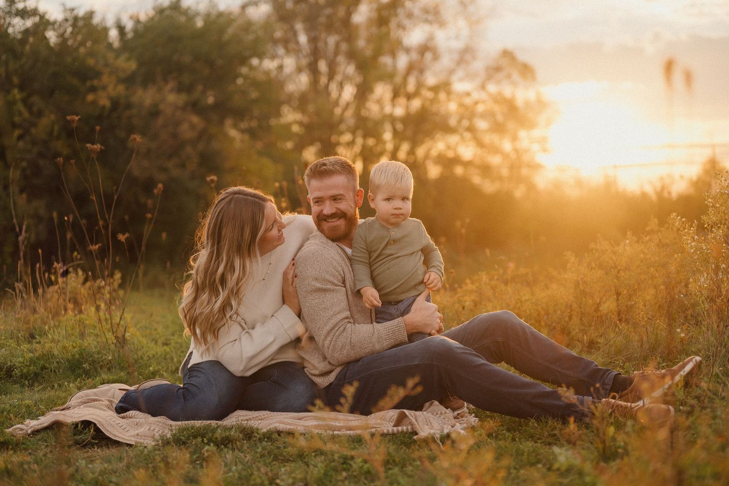 Family relaxing together on a blanket in a golden field during sunset with warm autumn lighting.