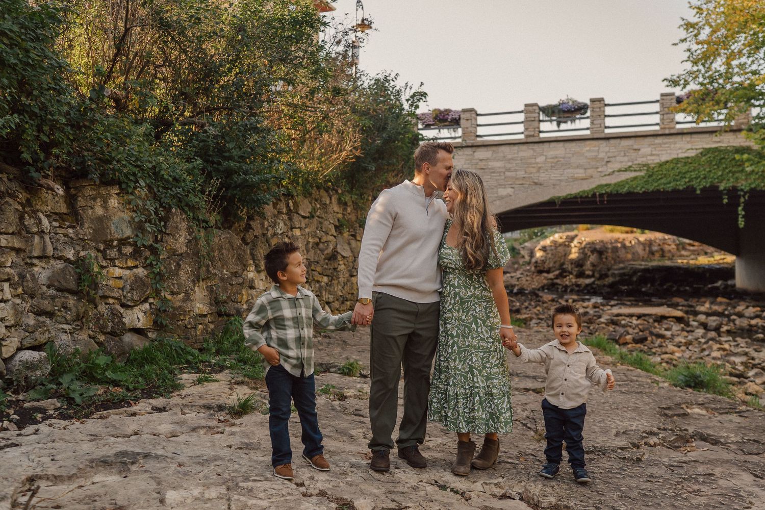 Family portrait session by a stone bridge with creek rocks and autumn foliage.