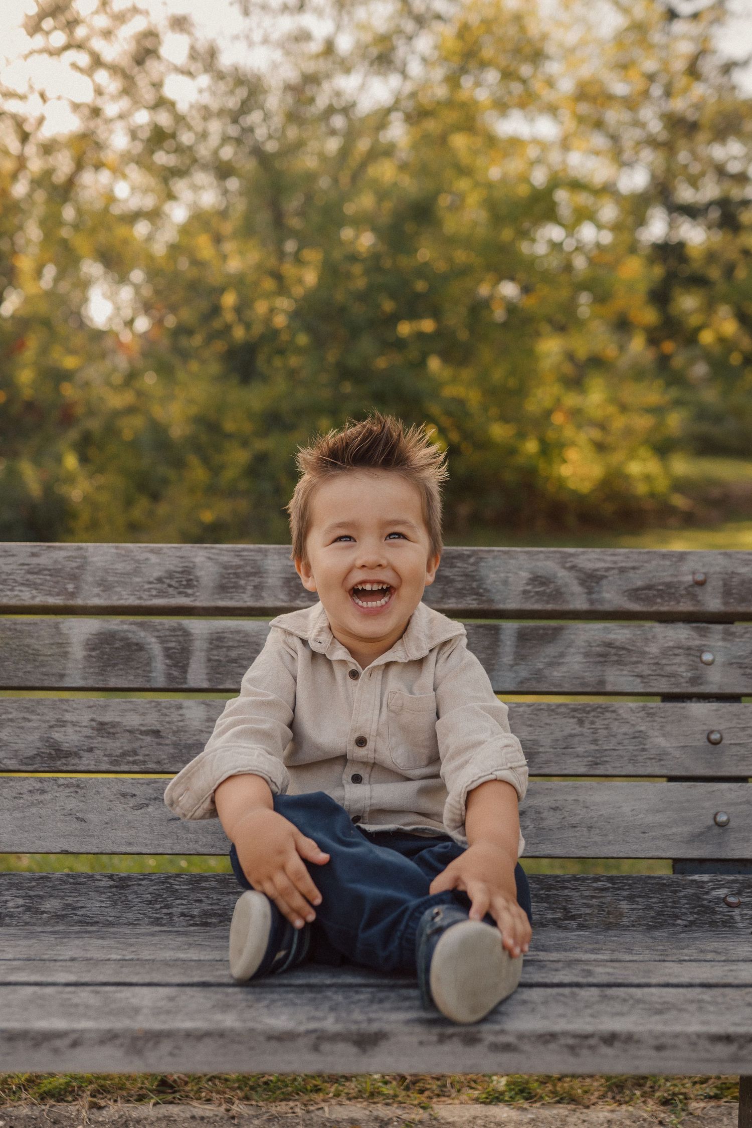 A joyful child sits on a wooden park bench during a golden autumn afternoon.
