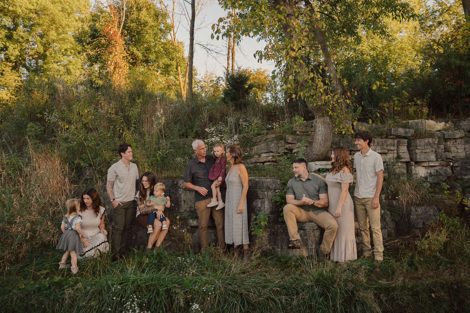Group of people gathered outdoors for casual portraits during golden hour with stone wall backdrop.