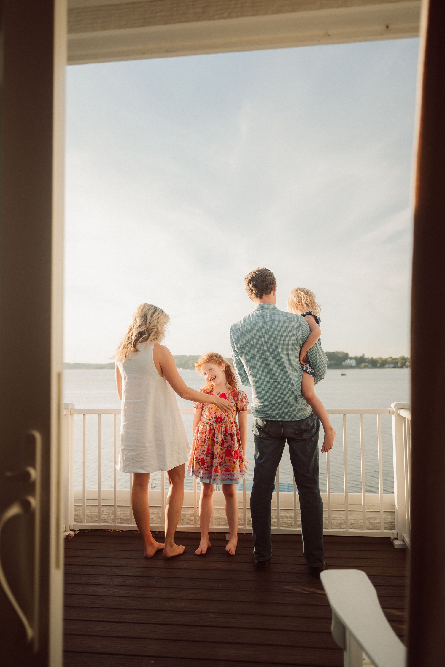 Family enjoying a sunset view together on a wooden deck overlooking the water.