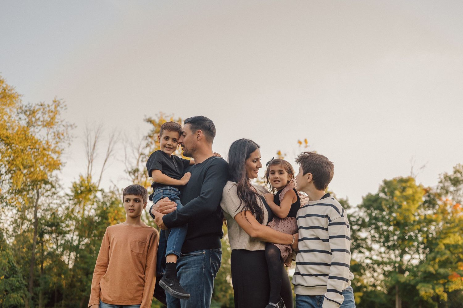 Group of friends dancing together in a park during sunset with trees in the background.
