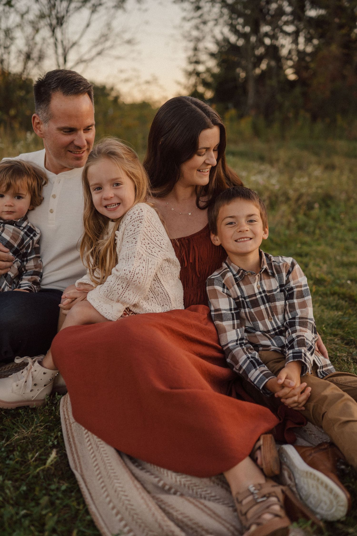 Family sits together on blanket during golden hour outdoor photo session.