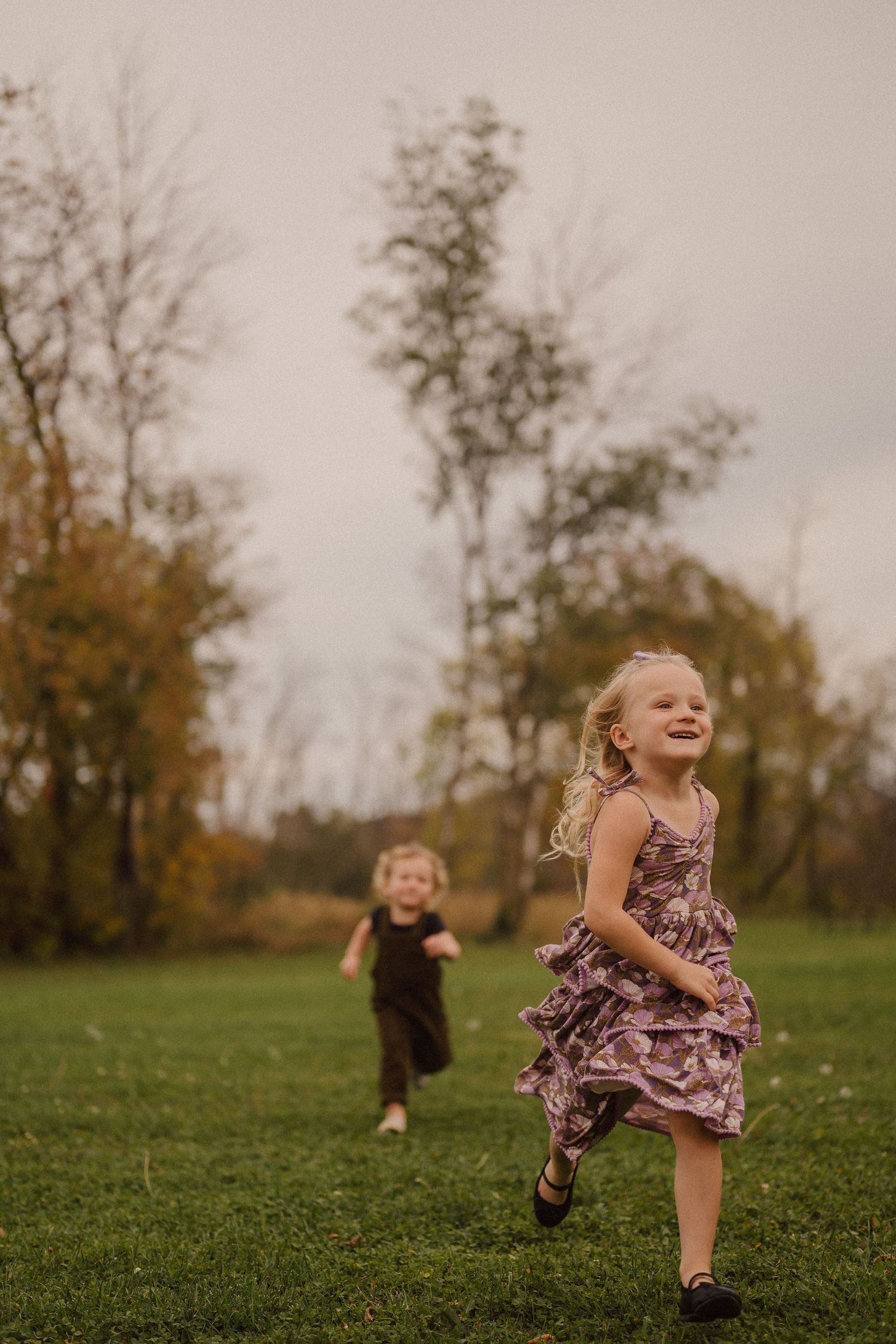 Children run and play in a grassy field on an autumn evening.