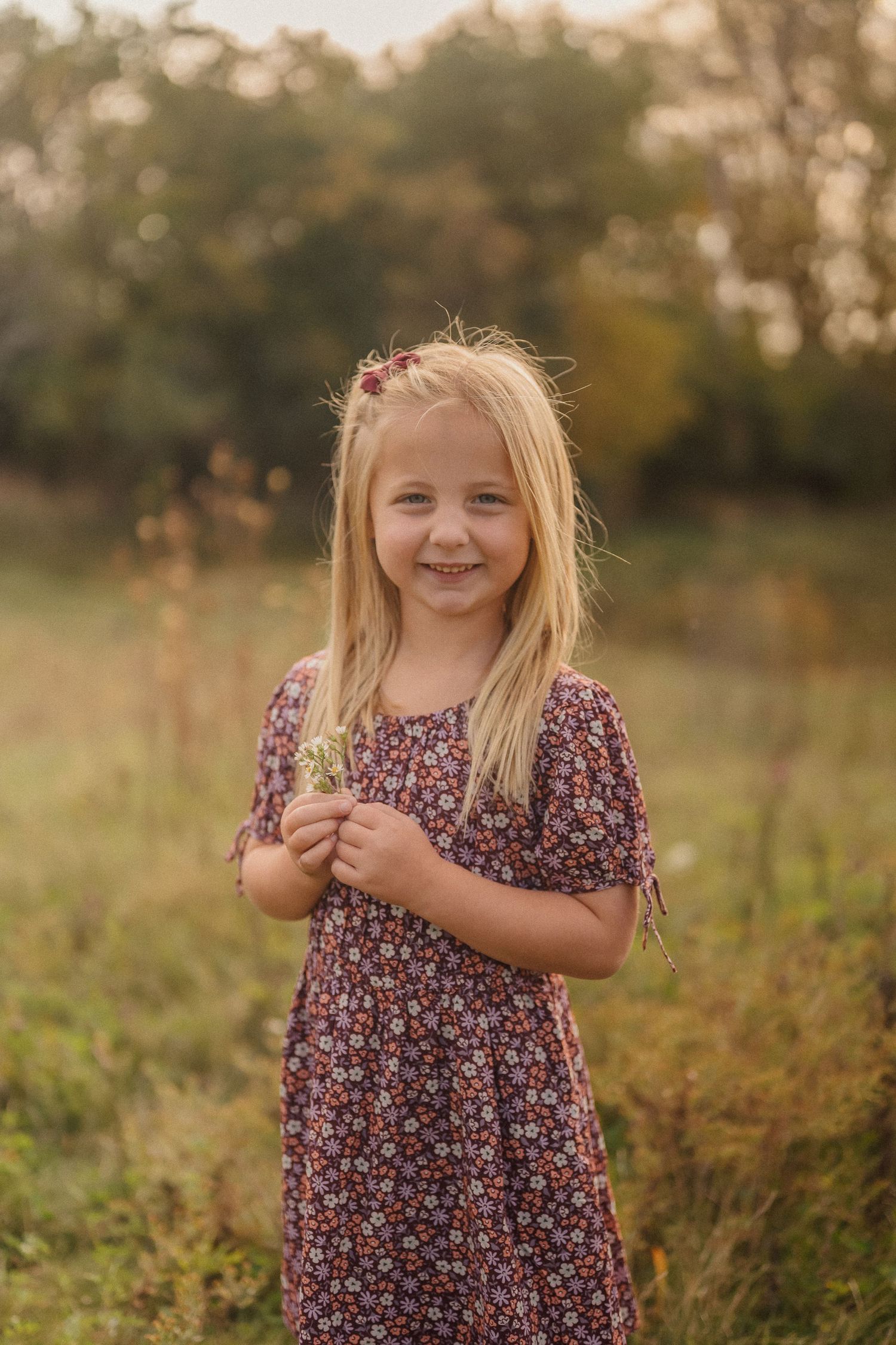 Young girl in floral dress poses playfully in a sunlit meadow during golden hour.