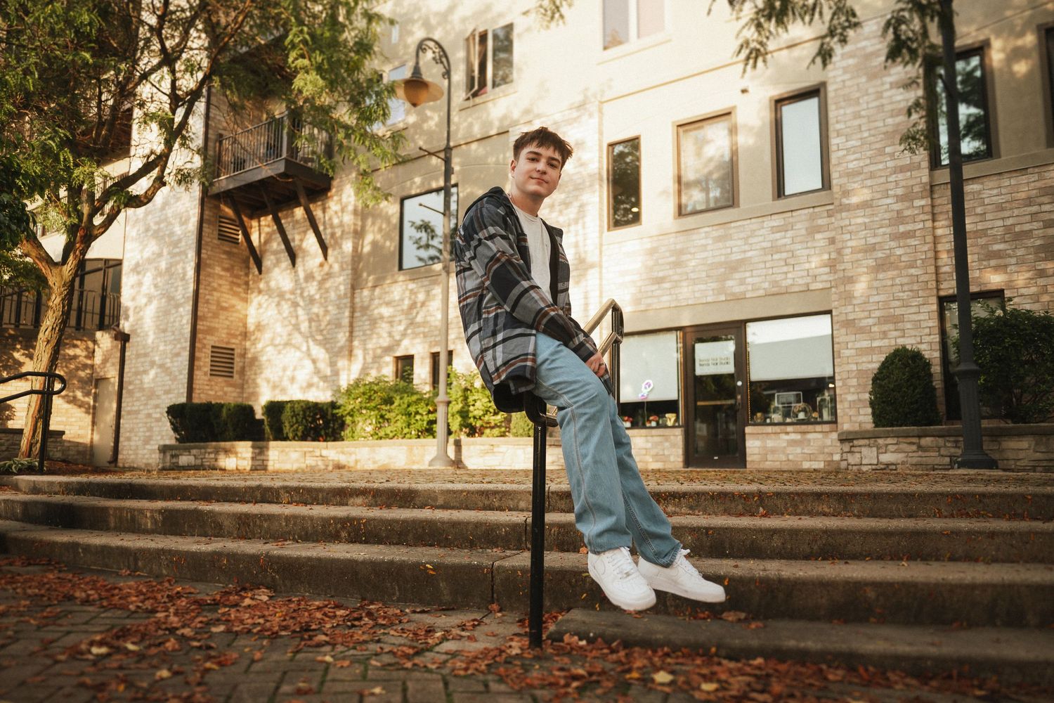 Skateboarder performs a trick sequence on concrete steps near a brick building in an urban setting.