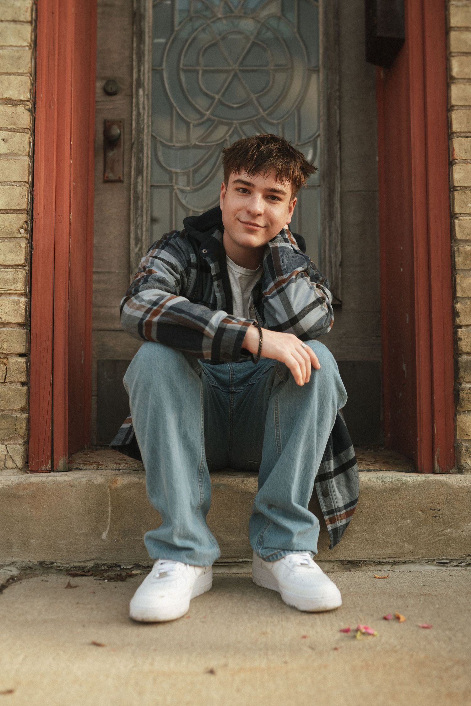 Someone sitting on stone steps in front of an ornate doorway wearing plaid and denim.