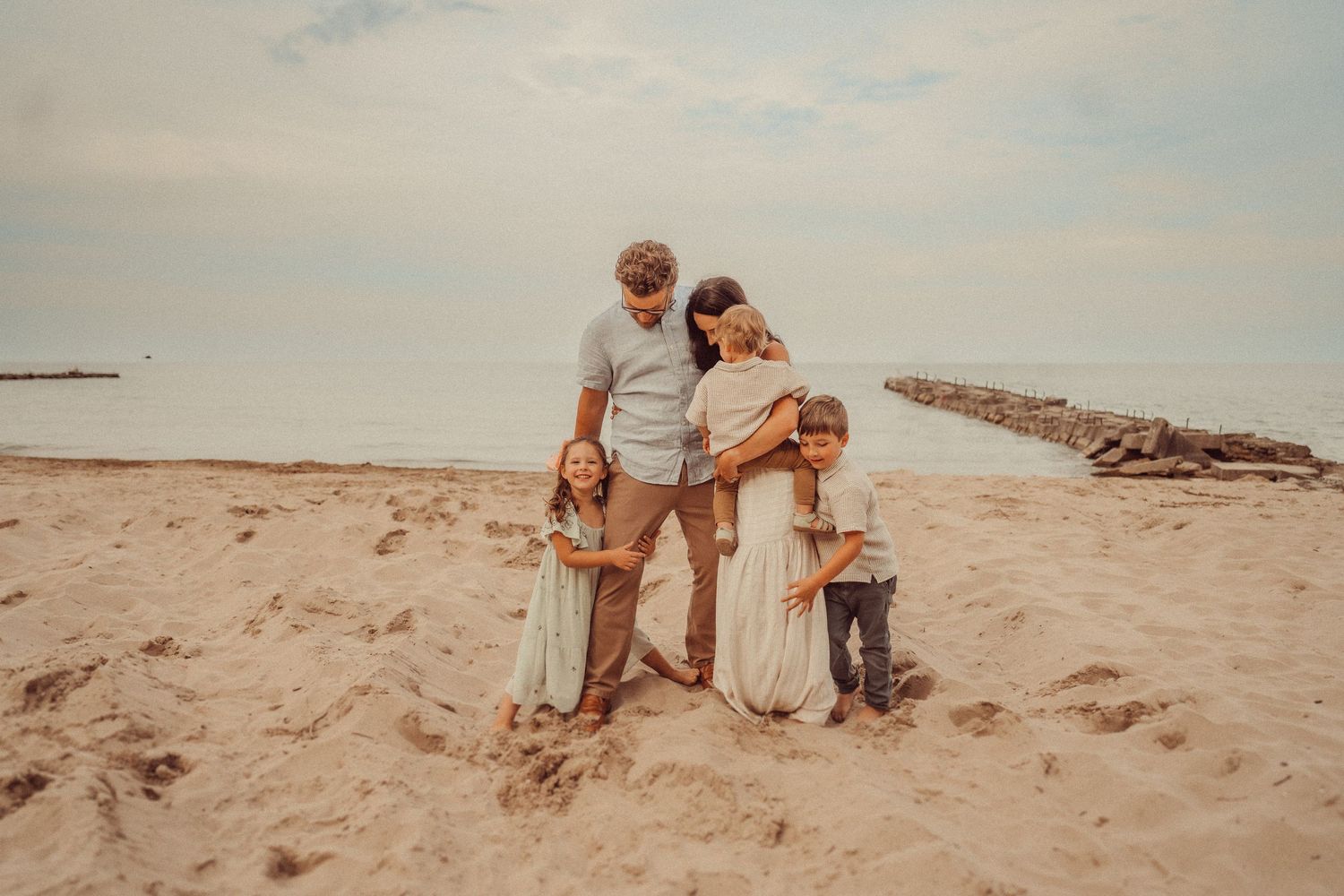 Family group embraces while standing on sunny beach.