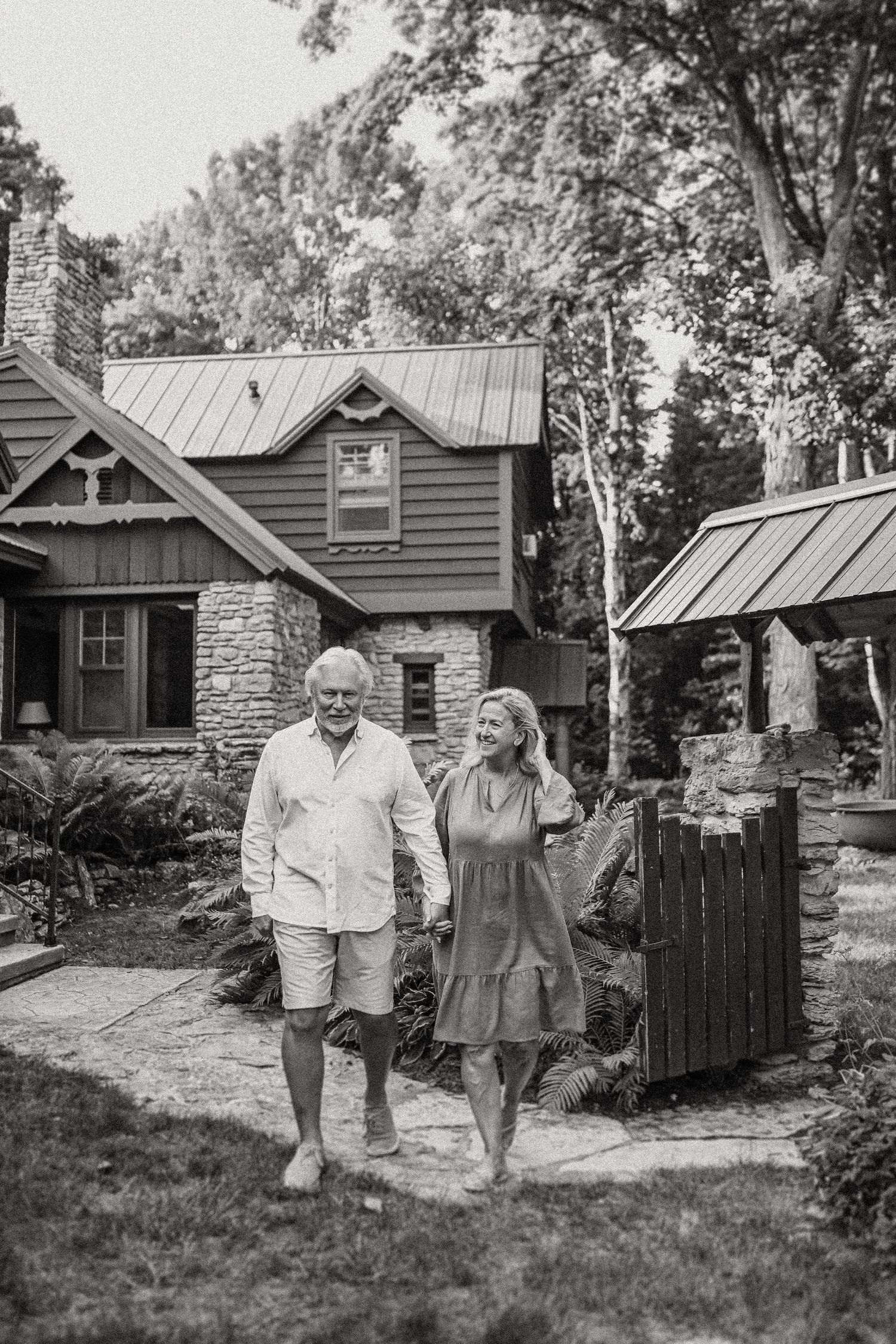 Couple walking hand in hand along garden path by rustic cabin with metal roof.