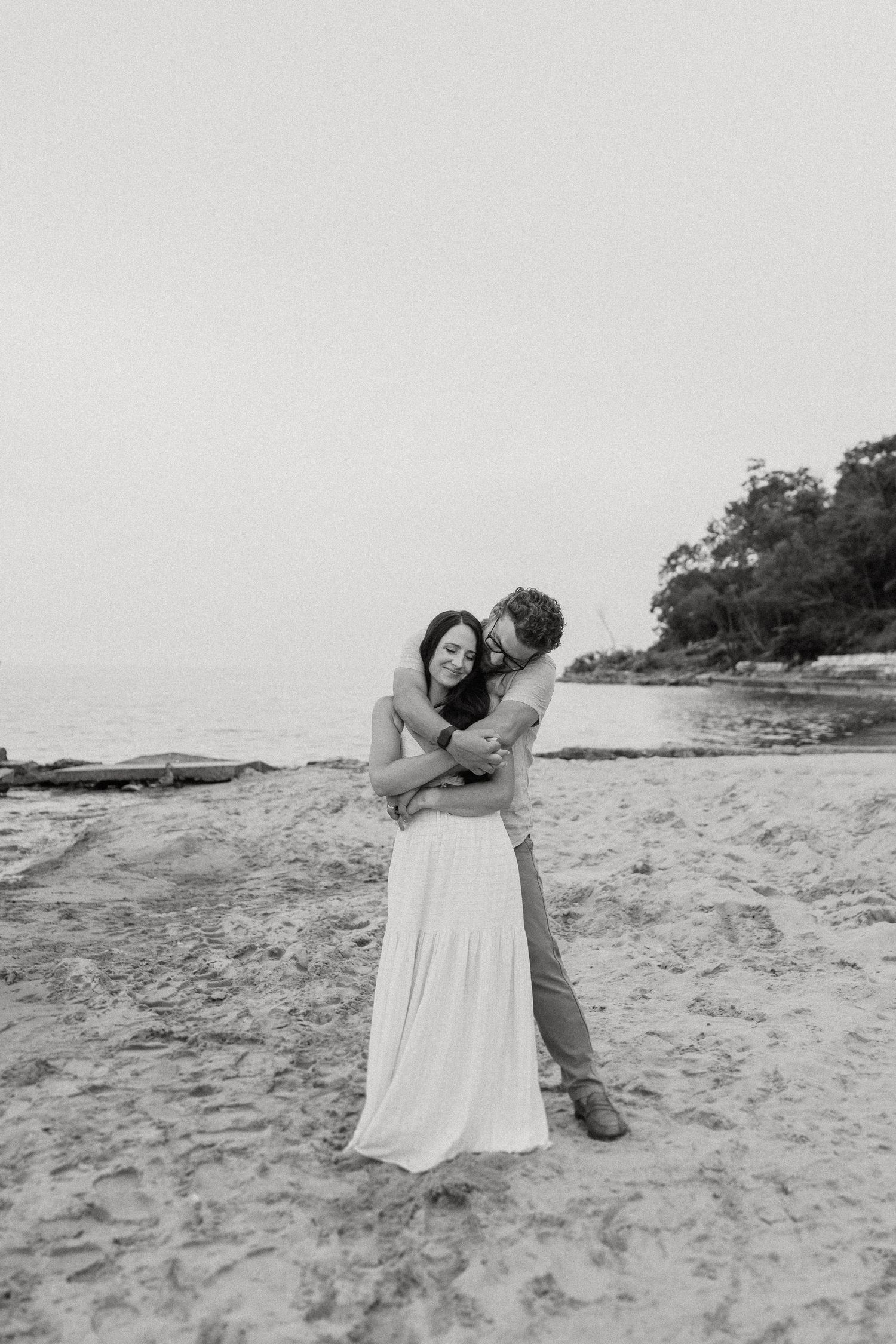Black and white portrait of couple embracing on rocky beach landscape.