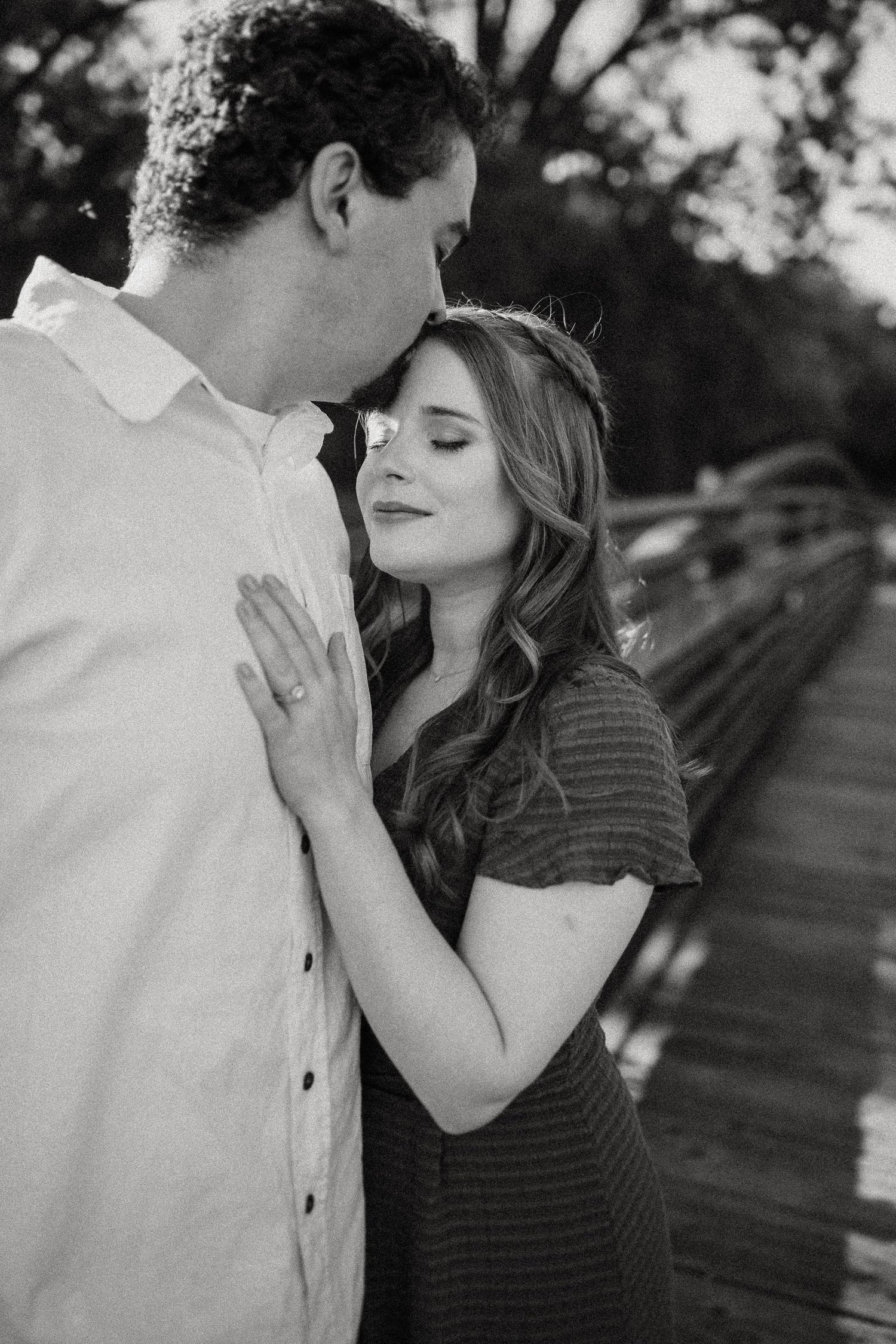 Intimate black and white portrait of a couple sharing a tender moment on a bridge.