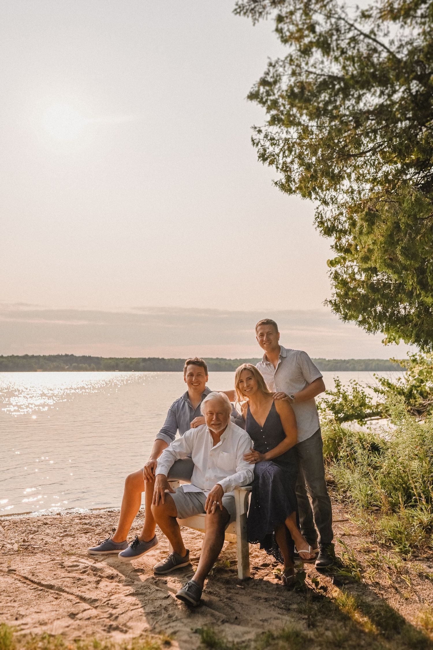 Golden hour family portrait at a lakeside beach with tree backdrop.