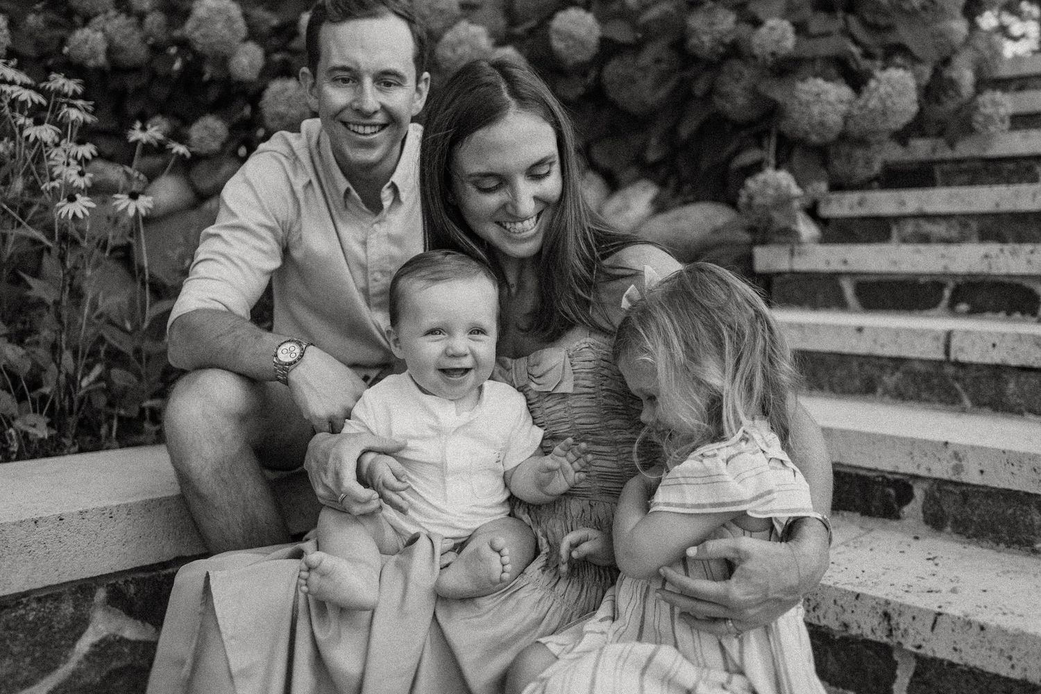 Family portrait on rustic stone steps with hydrangea bushes and flowers in background.