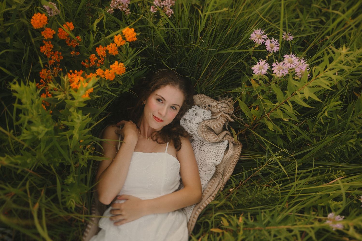 A white-clad figure rests in a garden setting surrounded by vibrant orange and pink flowers among lush greenery.
