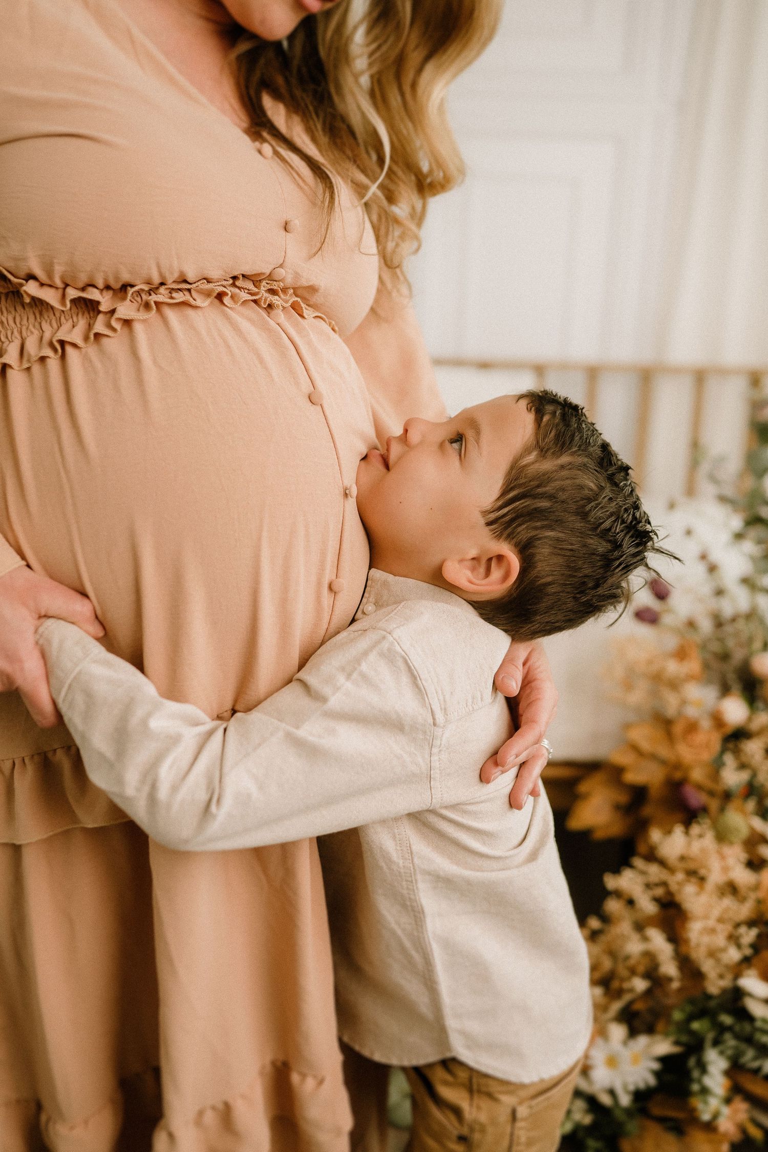 A series of tender mother and child hugging moments captured in warm, peachy tones with floral arrangements in the background.