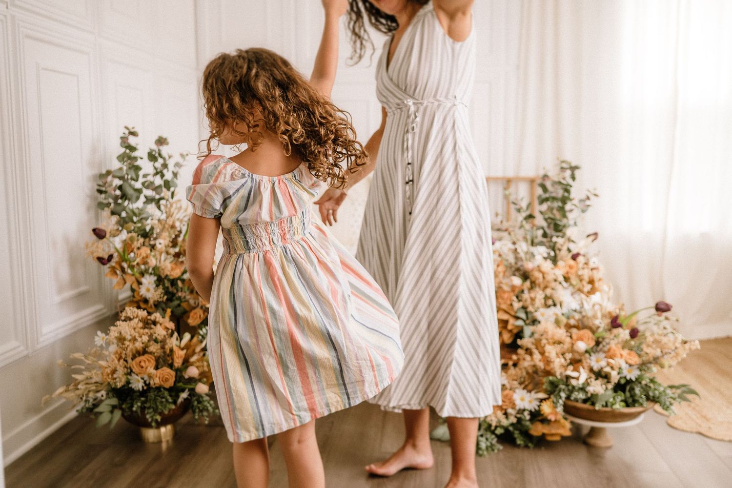Natural light portrait with floral arrangements and striped dresses against white walls.