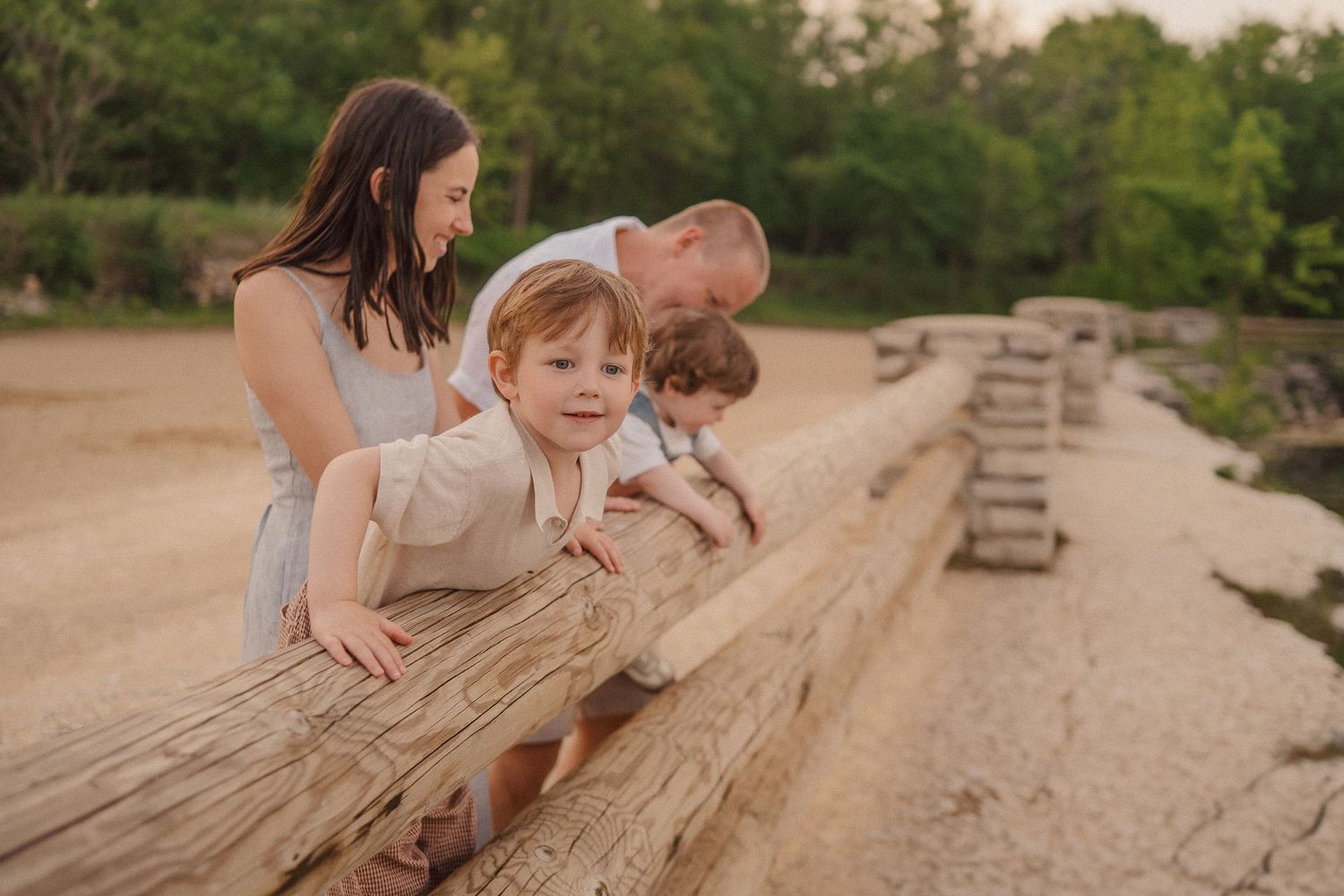 A family explores together while sitting on a wooden log in a natural outdoor setting.