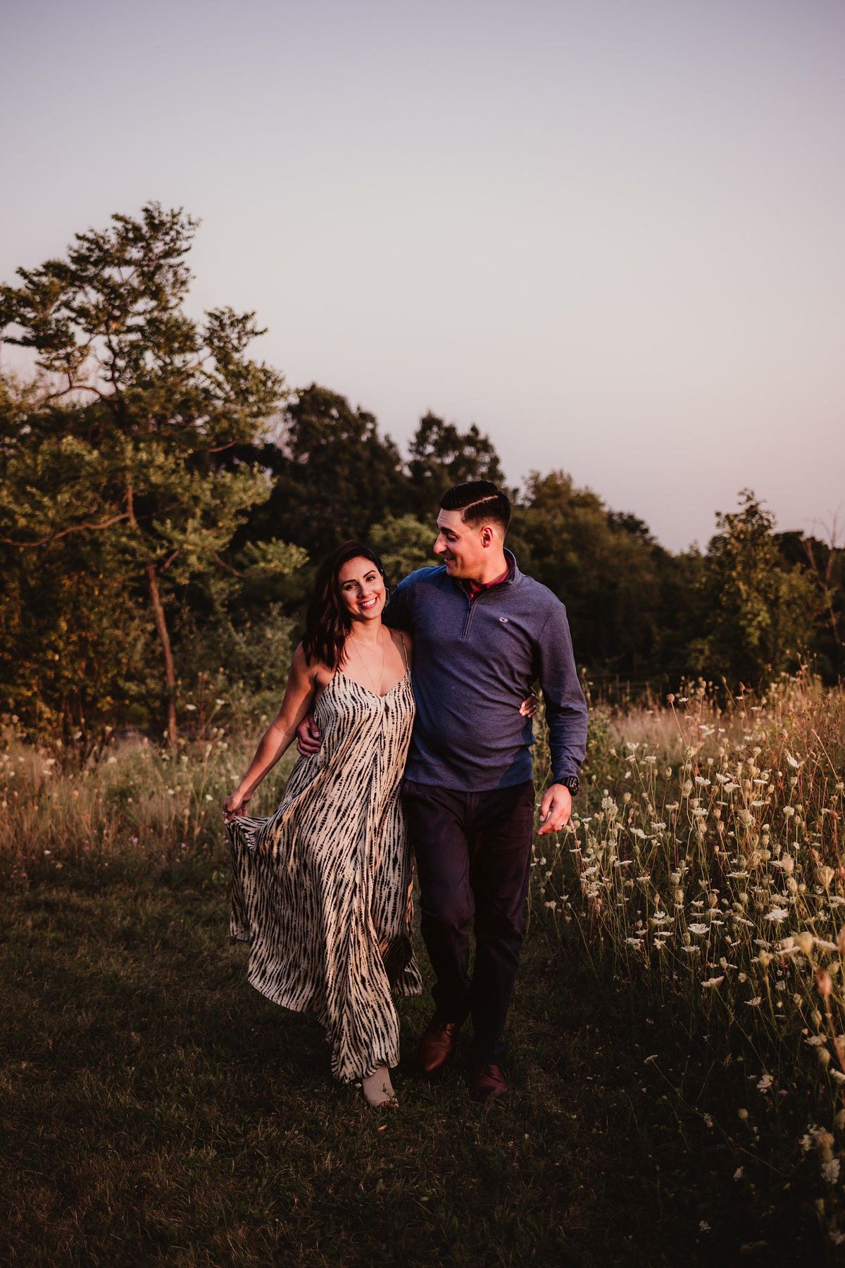 Couple walking through a meadow at dusk wearing coordinated outfits.