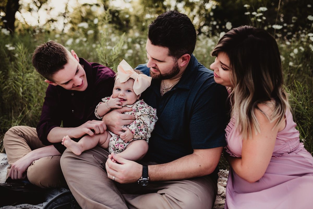 Family sitting together in a wildflower field at sunset with a baby wearing floral outfit.