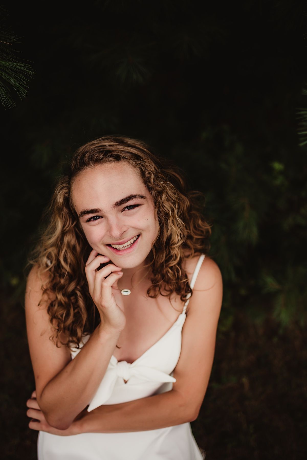 Close up portrait against dark foliage background with genuine smile.