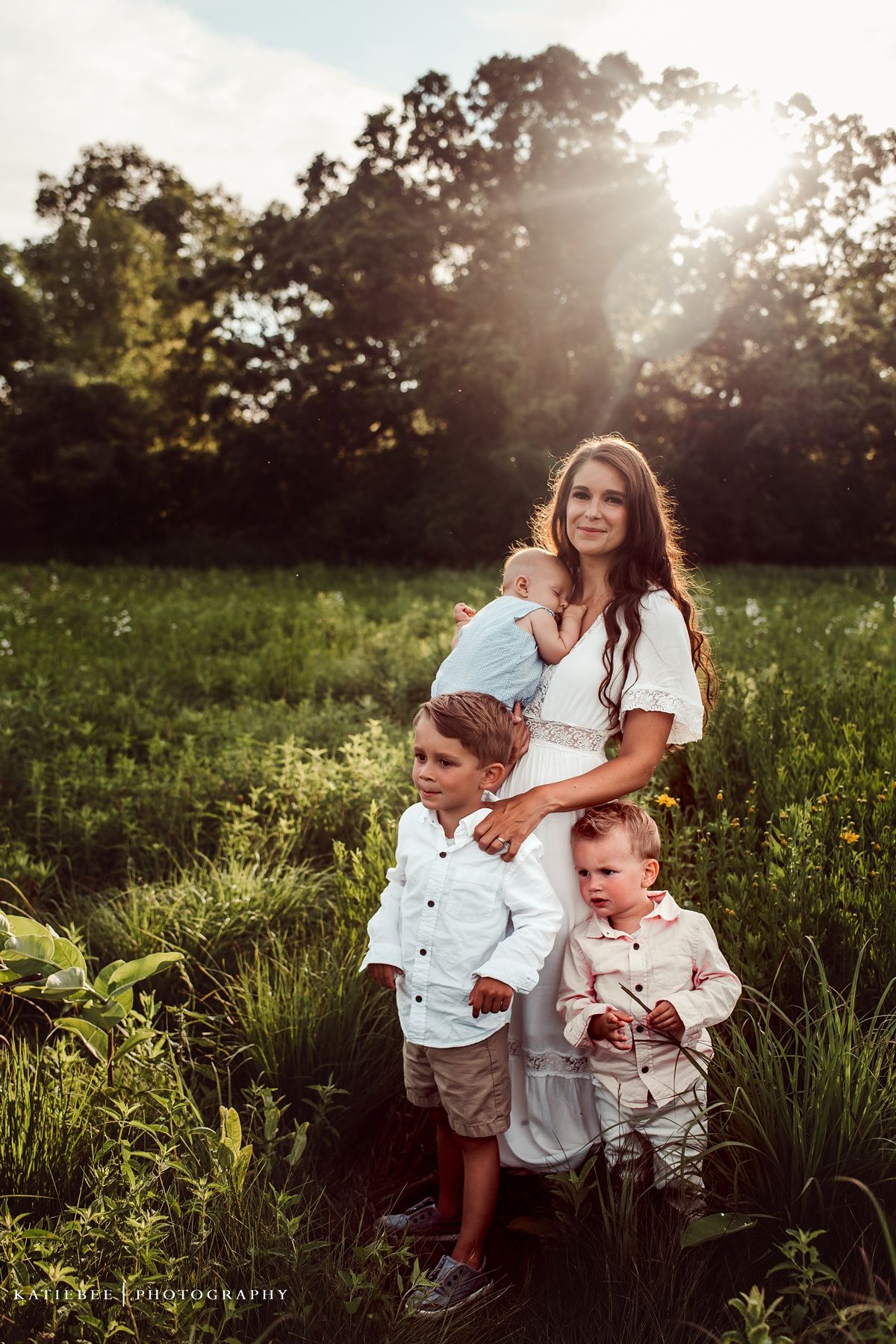 Family portrait in sun-drenched field with wildflowers during sunset.
