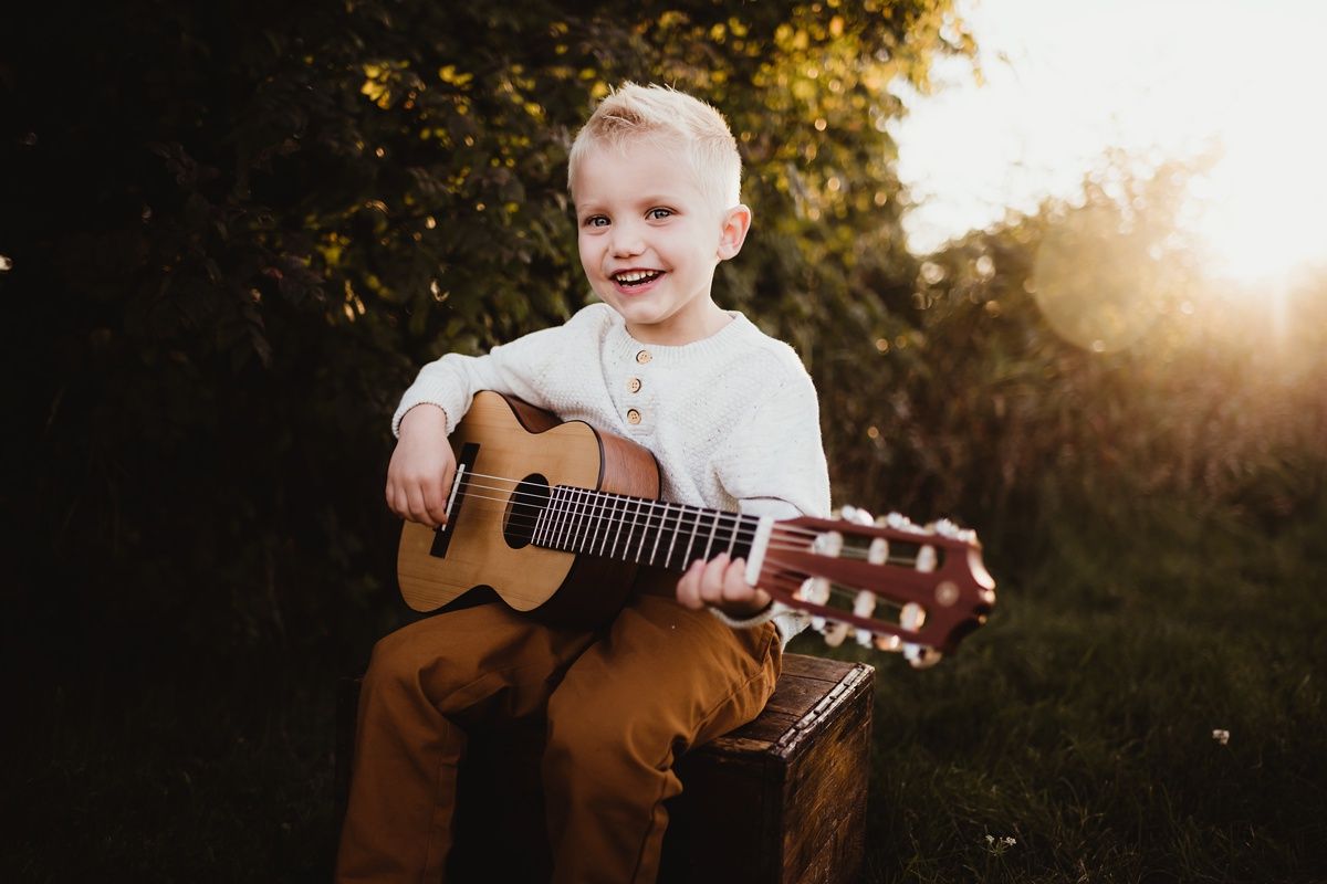 Young musician playing acoustic guitar outdoors during golden hour sunset.