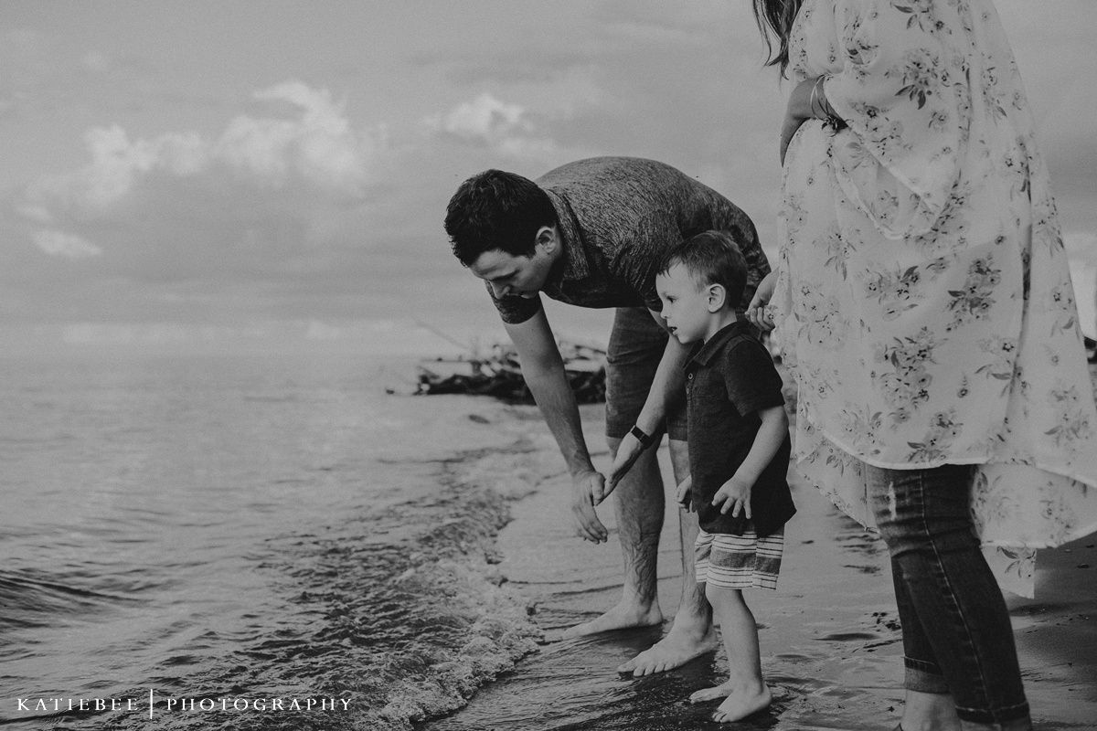 Black and white photo of family exploring the shoreline together at the beach.