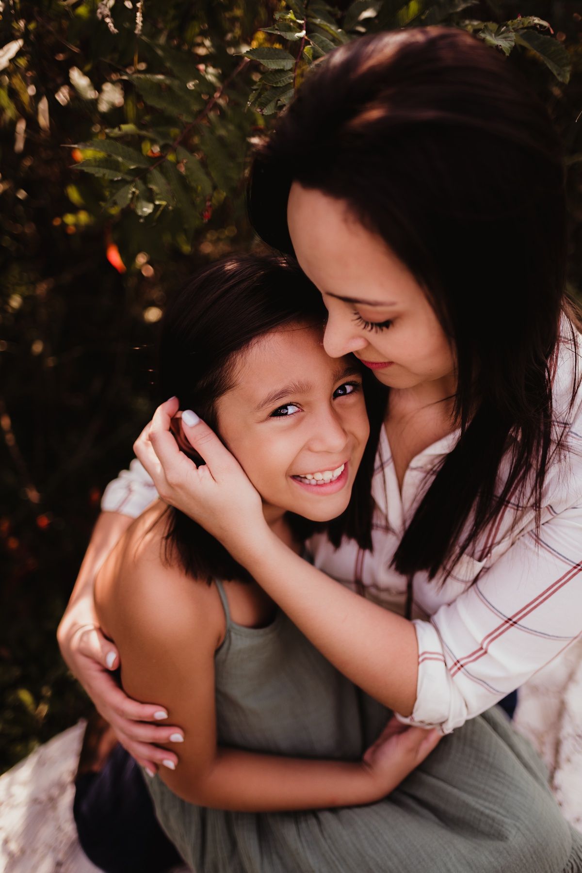 Sweet candid outdoor portrait showing a close embrace and happy smiles against greenery.