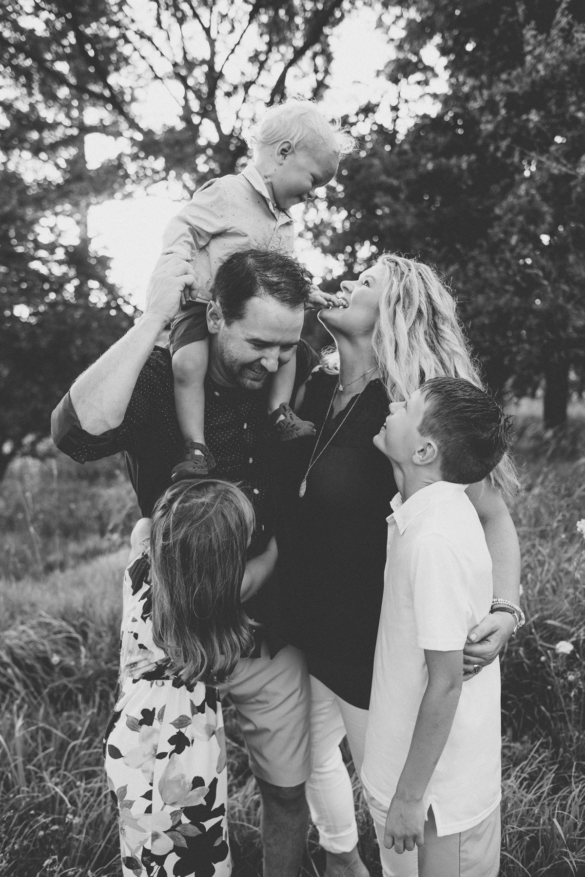 A black and white portrait of a loving family embracing outdoors.