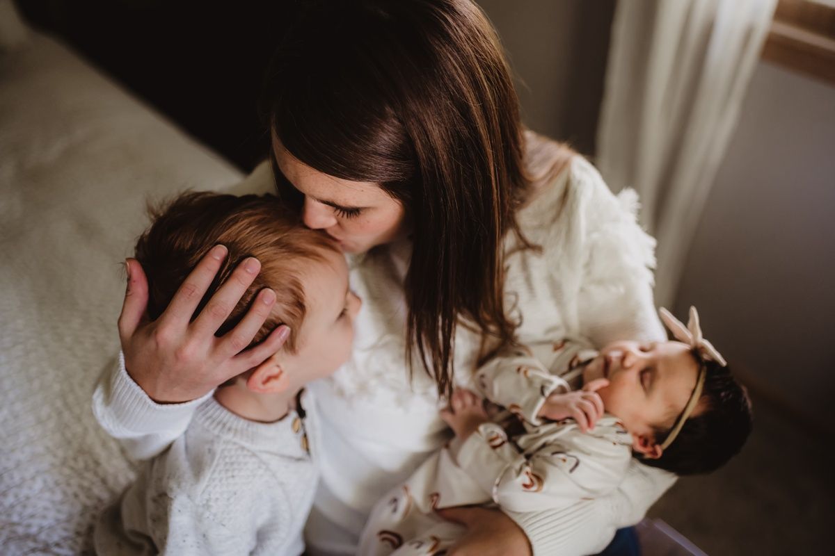 Intimate indoor portrait showing gentle affection with children in white clothing.