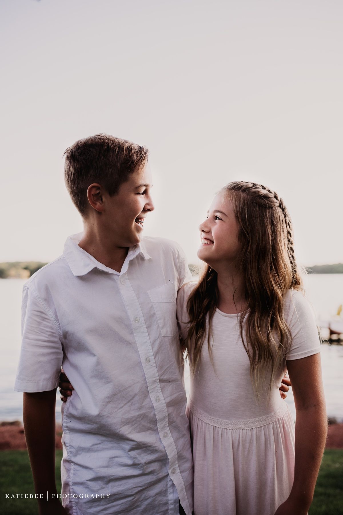 Two young people in white outfits sharing cheerful moment by the lake.