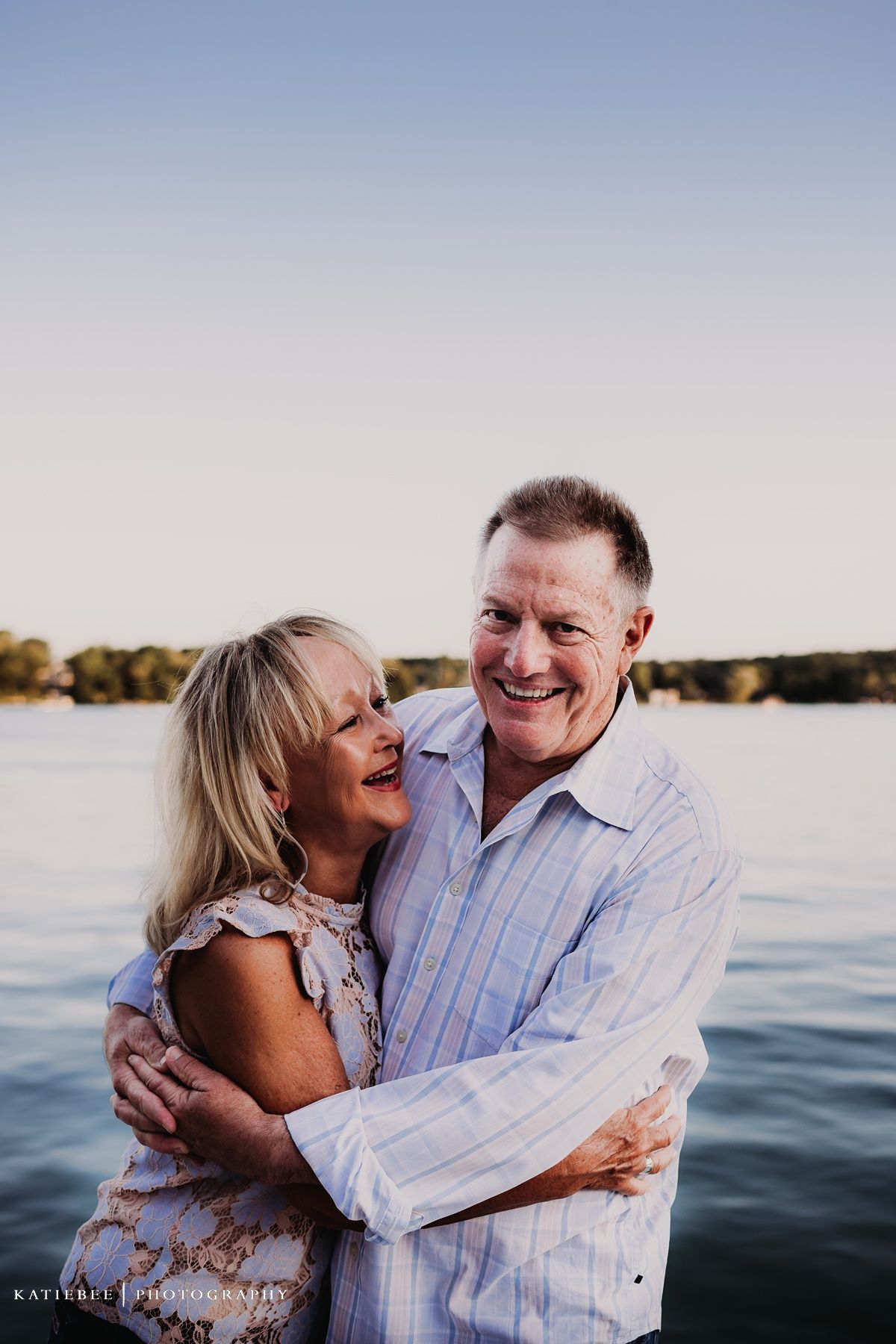 Happy couple embracing and laughing together by the waterfront at golden hour.