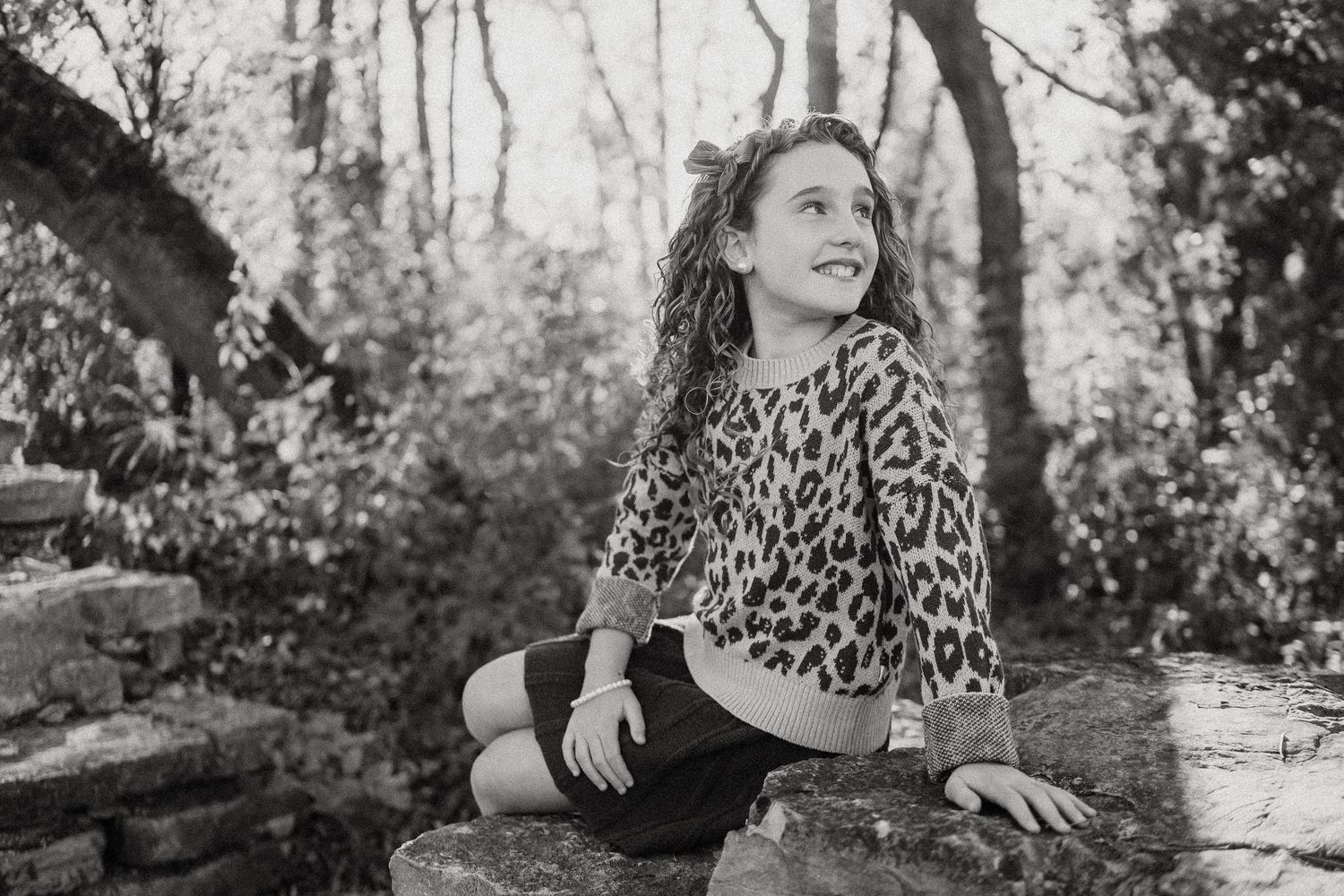 Black and white portraits capture joyful expressions while resting on a stone wall in a wooded setting.