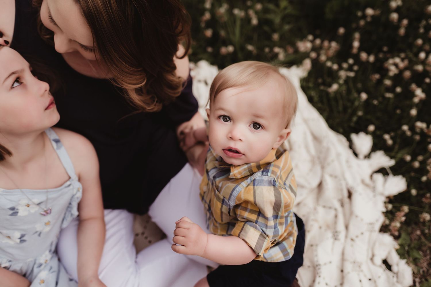 Close-up outdoor portrait of a young toddler and family members against a natural backdrop.