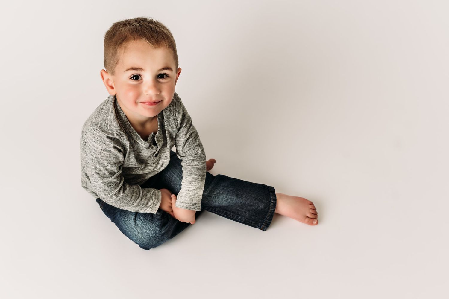 A relaxed pose sitting cross-legged on a white floor wearing casual attire.