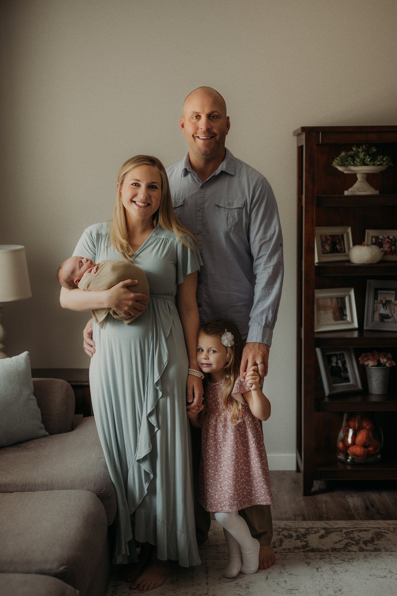 Family portrait in cozy living room with bookshelf and lamp in background.